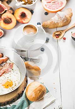 Fried egg with sausages and bacon, bread, croissants, coffee
