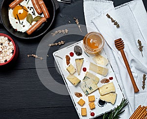 fried egg with sausages in a black round frying pan with a handle, a board with sliced different cheese