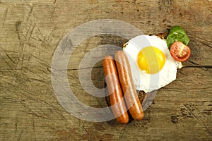 Fried egg with sausages and tomatoes with herbs on a piece of bread on a wooden table.