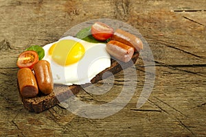 Fried egg with sausages and tomatoes on a piece of bread on a wooden table.