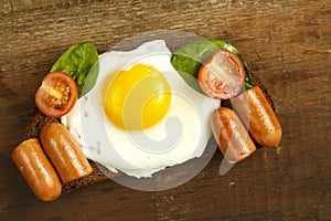 Fried egg with sausages and tomatoes on a piece of bread on a wooden table.