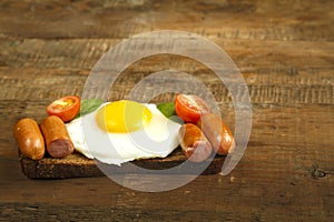 Fried egg with sausages and tomatoes on a piece of bread on a wooden table.