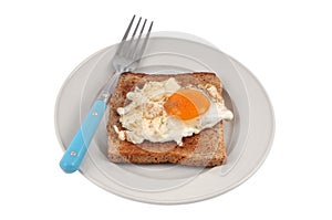 Fried egg on a slice of sandwich bread in a plate with a fork close-up on a white background