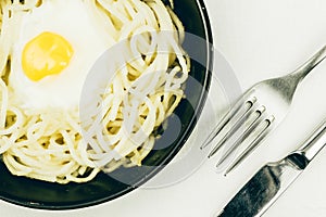 Fried egg and spaghetti in a black frying pan, fork and knife