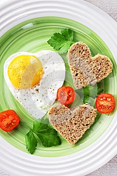 Fried egg and two slices of bread in the shape of a heart. Romantic Breakfast for Valentine`s day