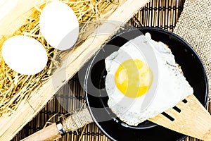 Fried egg on a wooden spatula over a frying pan.