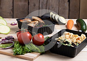 Fried eggplants in container with grilled chicken wings and raw vegetables on rustic background, cherry tomato  and micro greenss