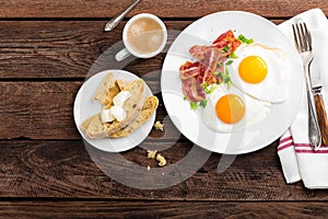 Fried eggs, bacon and italian ciabatta bread on white plate. Cup of coffee. Breakfast. Top view. Wooden background