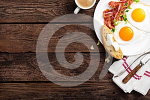 Fried eggs, bacon and italian ciabatta bread on white plate. Cup of coffee. Breakfast. Top view. Wooden background