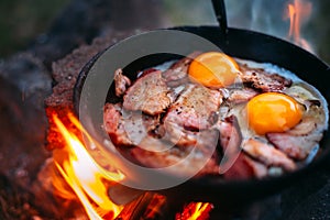 Fried eggs with bacon in a pan in the forest. Food at the camp. Fried egg with bacon on fire. Picnic