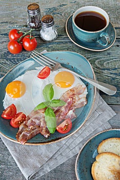 Fried eggs, bacon, tomato, toast and a cup of coffee