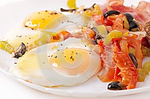 Fried eggs with bacon, tomatoes, olives and slices of cheese