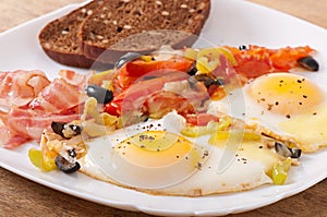 Fried eggs with bacon, tomatoes, olives and slices of cheese