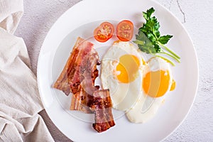 Fried eggs and bacon, tomatoes and parsley on a plate. Homemade breakfast. Top view. Closeup