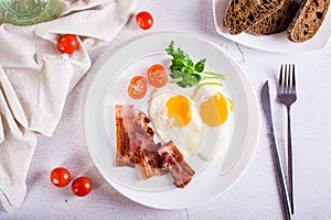 Fried eggs and bacon, tomatoes and parsley on a plate on the table. Homemade breakfast. Top view