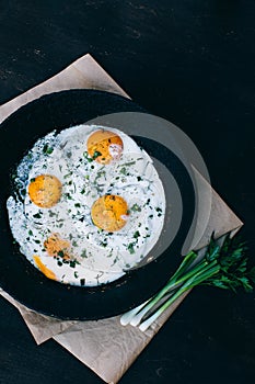 Fried eggs in cast iron frying pan on dark wooden background