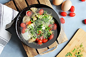 Fried eggs with cherry tomatoes, potatoes and onions in a pan on a wooden stand on the table