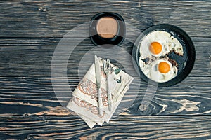 fried eggs and a cup of coffee with milk for breakfast on an old wooden background. top view