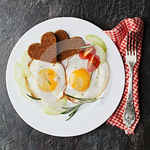 Fried eggs with fresh vegetables and toast in shape of heart on white plate