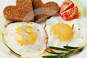 Fried eggs with fresh vegetables and toast in shape of heart on white plate