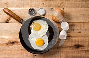 Fried eggs, in a frying pan, on wooden background. Top wiew