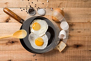 Fried eggs, in a frying pan, on wooden background. Top wiew