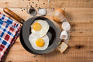 Fried eggs, in a frying pan, on wooden background. Top wiew