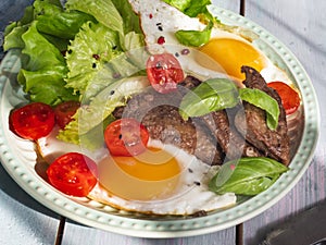 Fried eggs with green salad, cherry tomatoes and fried beef liver close up shot