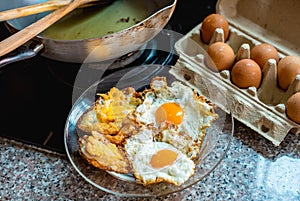 Fried eggs in kitchen with fresh raw egg and a pan in background