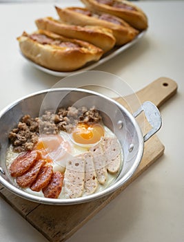 Fried eggs in a pan with meat on the wooden plate. The famous breakfast with Banh Mi - Vietnamese bun with meat