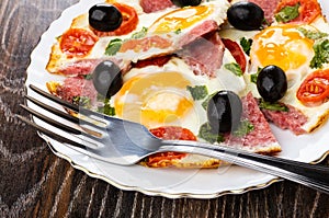 Fried eggs with sausages, tomato, black olives and fork in plate