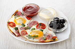 Fried eggs with sausages, tomato, ketchup, mayonnaise, olives in