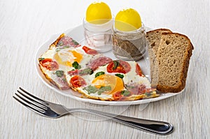 Fried eggs with sausages, tomato, salt and pepper, bread in plat