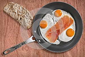 Fried Eggs and Smoked Ham Rasher in Frying Pan with Slice of Bread on Cherry Wood Background