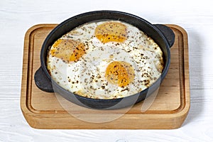 Fried eggs with spices in a small cast-iron pan, on a wooden stand