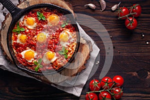 Fried eggs with tomatoes and vegetables. Shakshuka in a cast iron portioned pan on a wooden background top view