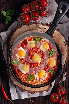 Fried eggs with tomatoes and vegetables. Shakshuka in a cast iron portioned pan on a wooden background top view