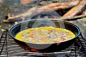 Fried eggs with vegetables are cooked in a pan on a grill on coals in the open air