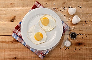 Fried eggs, on a white plate, on wooden background. Top Wiew