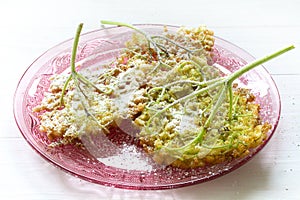 Fried elderflower pancakes with powdered sugar on a pink glass d photo