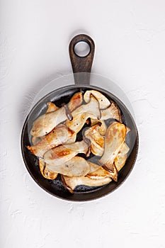 Fried eryngii mushrooms in cast-iron pan on white table. Grilled slices of king oyster mushrooms. Top view, copy space