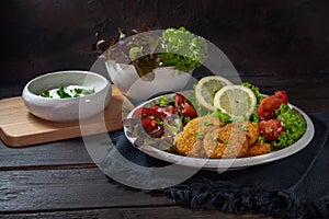 Fried falafel from chickpeas, sesame seeds, spices and herbs, served with salad and a yogurt dip on a rustic wooden table against