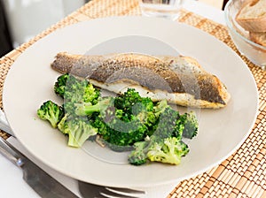 Fried fillet of sea bass with garnish of broccoli on black warm stone plate