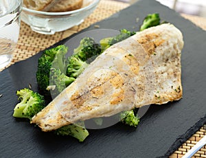 Fried fillet of sea bass with garnish of broccoli on black warm stone plate