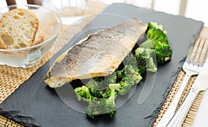 Fried fillet of sea bass with garnish of broccoli on black warm stone plate