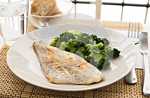 Fried fillet of sea bass with garnish of broccoli on black warm stone plate