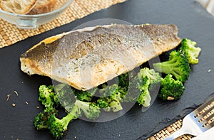 Fried fillet of sea bass with garnish of broccoli on black warm stone plate