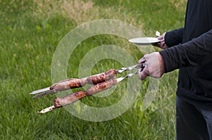 Fried on fire sausages on skewers in the hands of a man in a black jacket. Grilled meat.