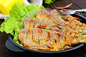 Fried fish carp sazan on a cast-iron frying pan with lettuce leaves
