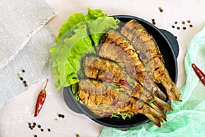 Fried fish carp sazan on a cast-iron frying pan with lettuce leaves